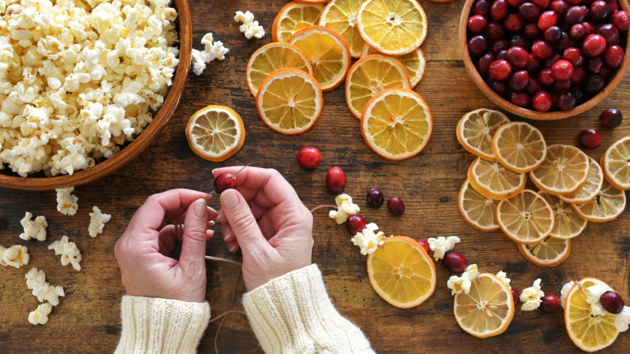 Female making Christmas garland by stringing popcorn, cranberries, dried orange and lemon slices on twine.
