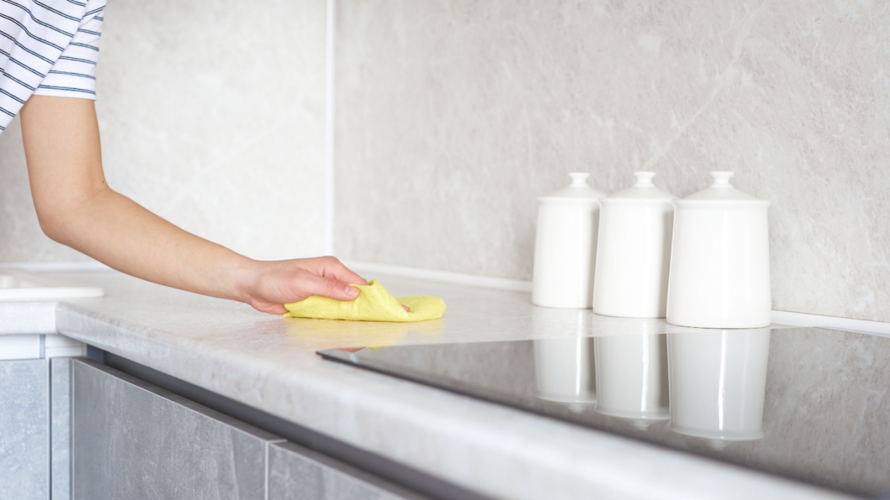 Woman removes dirt from the work surface with a soft rag. Female hand cleaning the countertop with a yellow cloth without detergent.