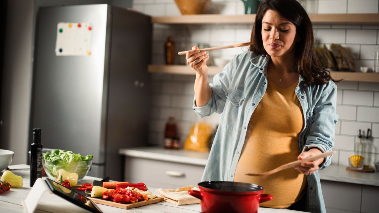 Beautiful pregnant woman preparing delicious food. Smiling woman cooking pasta at home