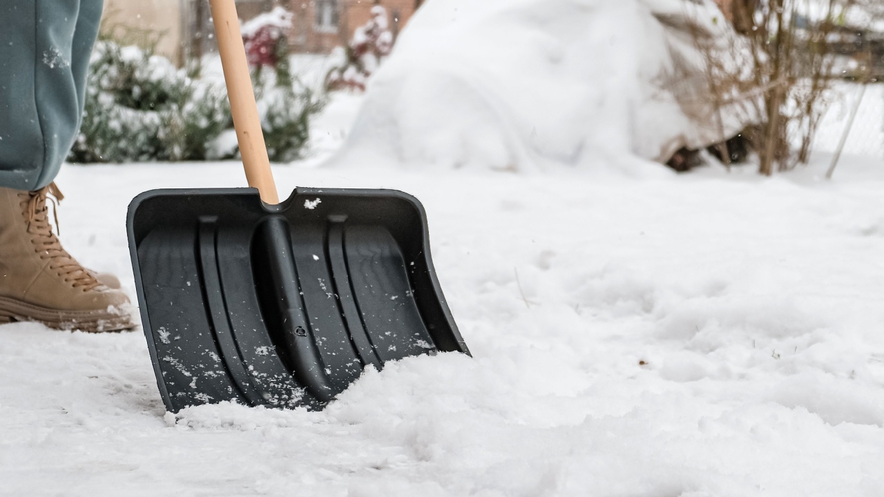 Close-up of a woman cleaning and clearing snow in front of the house on a sunny and frosty day. Cleaning the street from snow on a winter day. Snowfall, and a severe snowstorm in winter. 