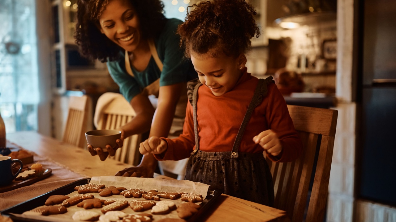 Happy African American mother and daughter enjoying in making gingerbread cookies for holidays in the kitchen. Focus is on girl.