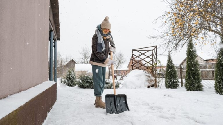 Close-up of a woman cleaning and clearing snow in front of the house on a sunny and frosty day. Cleaning the street from snow on a winter day. Snowfall, and a severe snowstorm in winter.