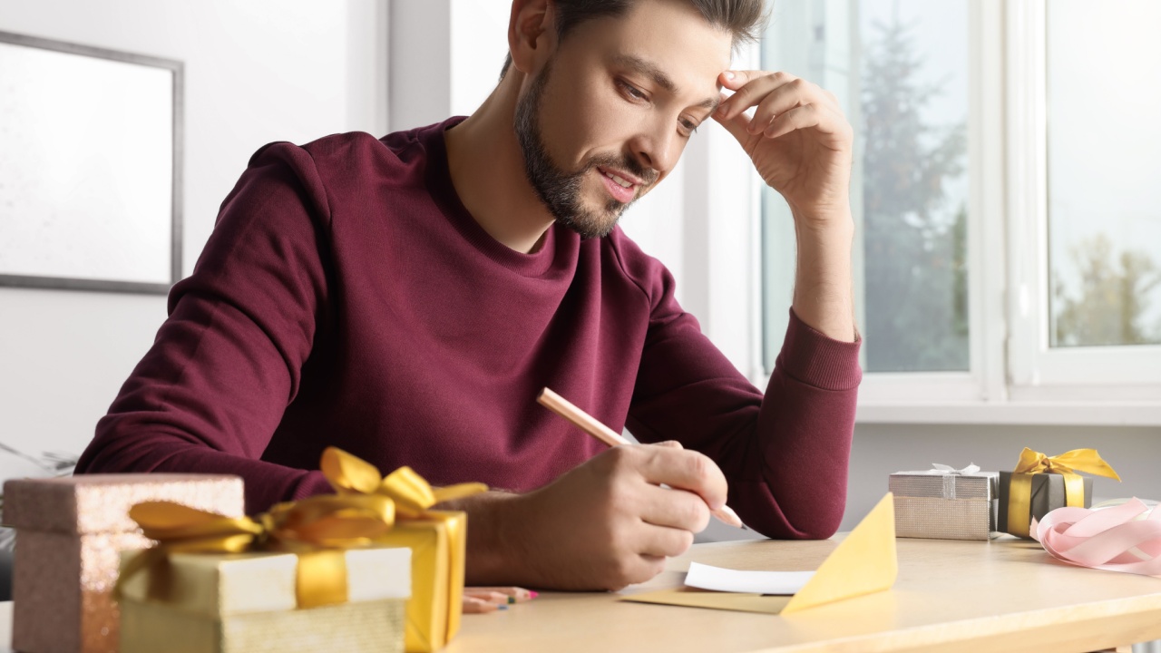 Man writing message in greeting card at wooden table in room
