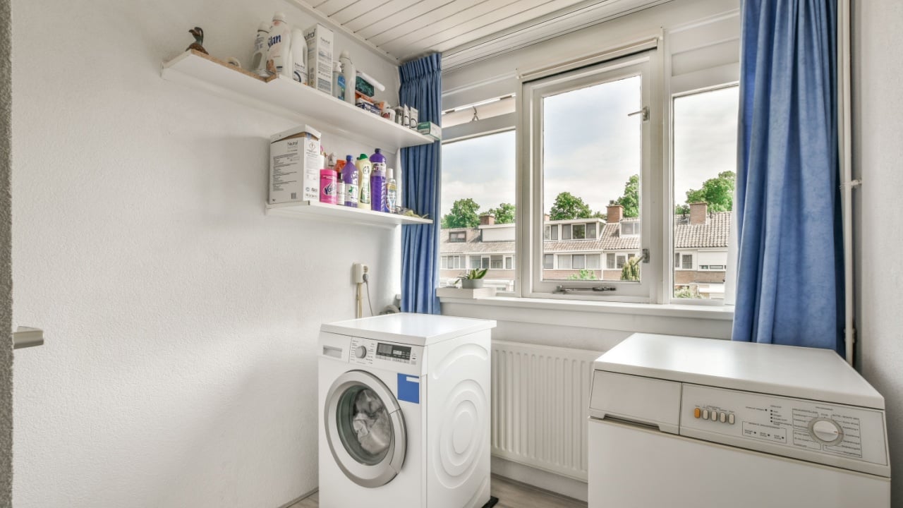Amsterdam, Netherlands - 10 April, 2021: a small laundry room with a washer and dryer in the corner, next to a window that has blue curtains