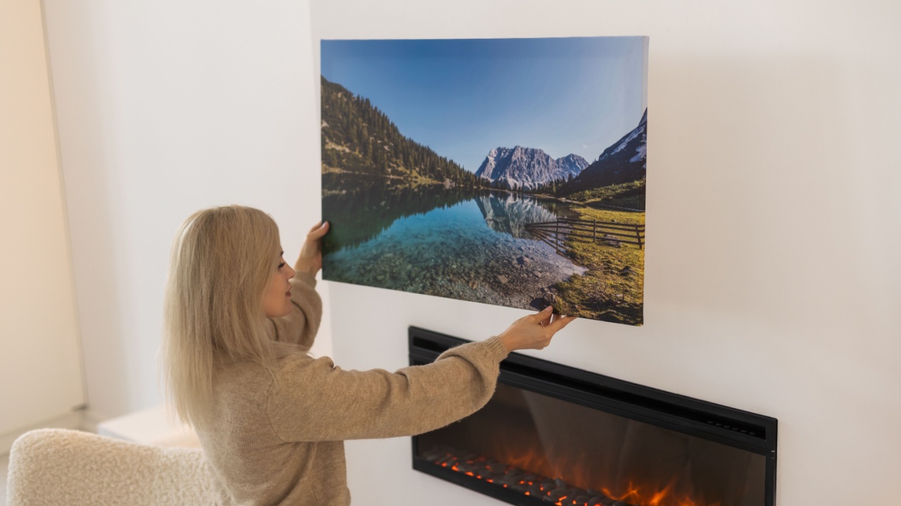 Modern Home Interior And Domestic Decor. Smiling young woman hanging painting, putting photo picture frame on the wall. Casual lady taking care of coziness in her new stylish apartment, profile