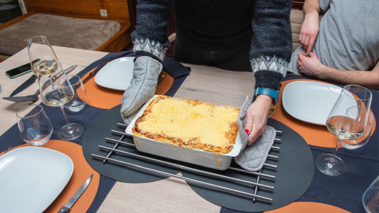Woman cut with knife hot tasty home baking lasagna in ceramic casserole dish