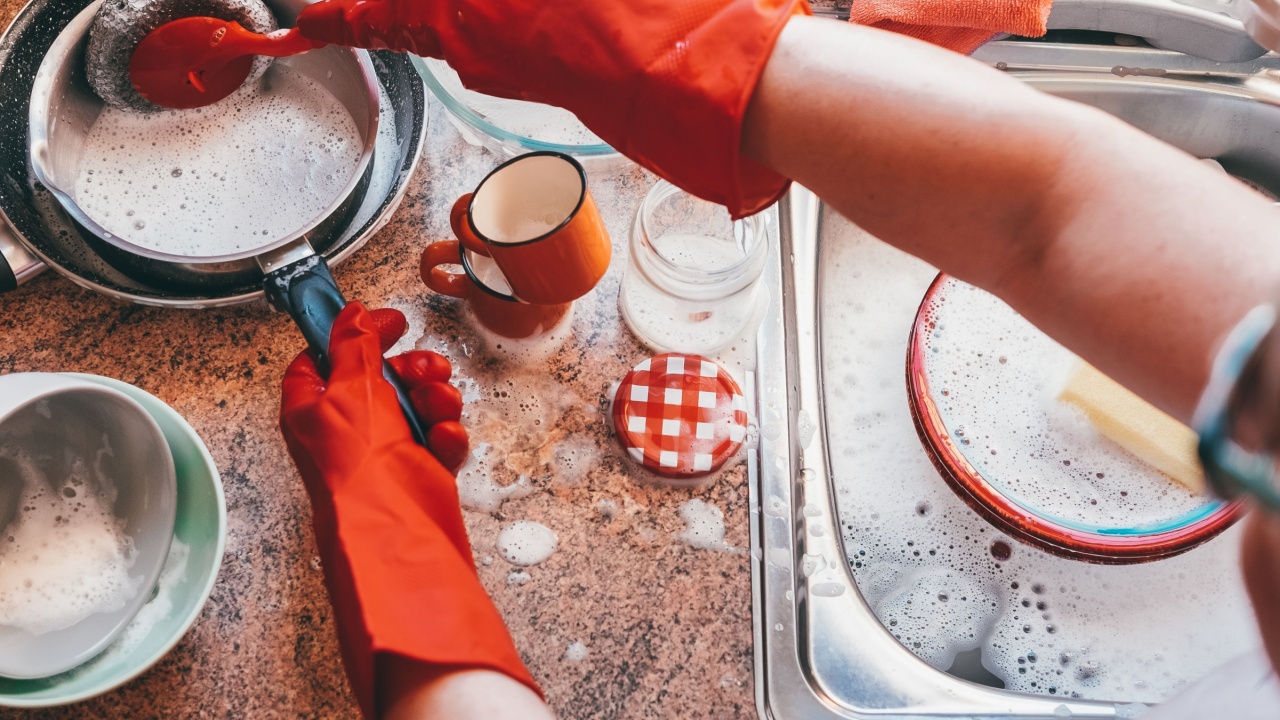 Housewife washing dishes in the kitchen sink. Senior woman washing crockery in front to the window, wearing red protective gloves.