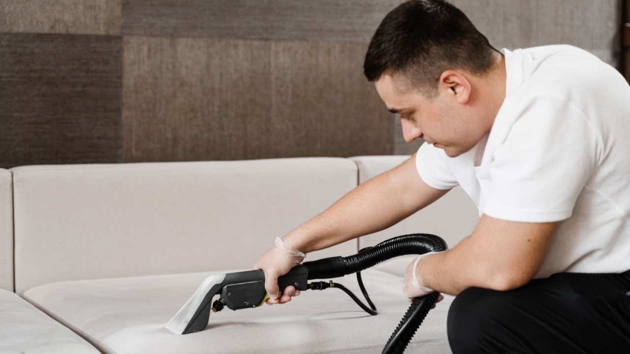 Housekeeper is extracting dirt from upholstered sofa using dry cleaning extraction machine. Cleaner is cleaning couch with washing vacuum cleaner extractor machine for dry clean upholstered furniture