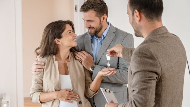 A couple of homeowners getting key to a new house apartment from a realtor, happy real estate owners make a purchase deal, family mortgage investment