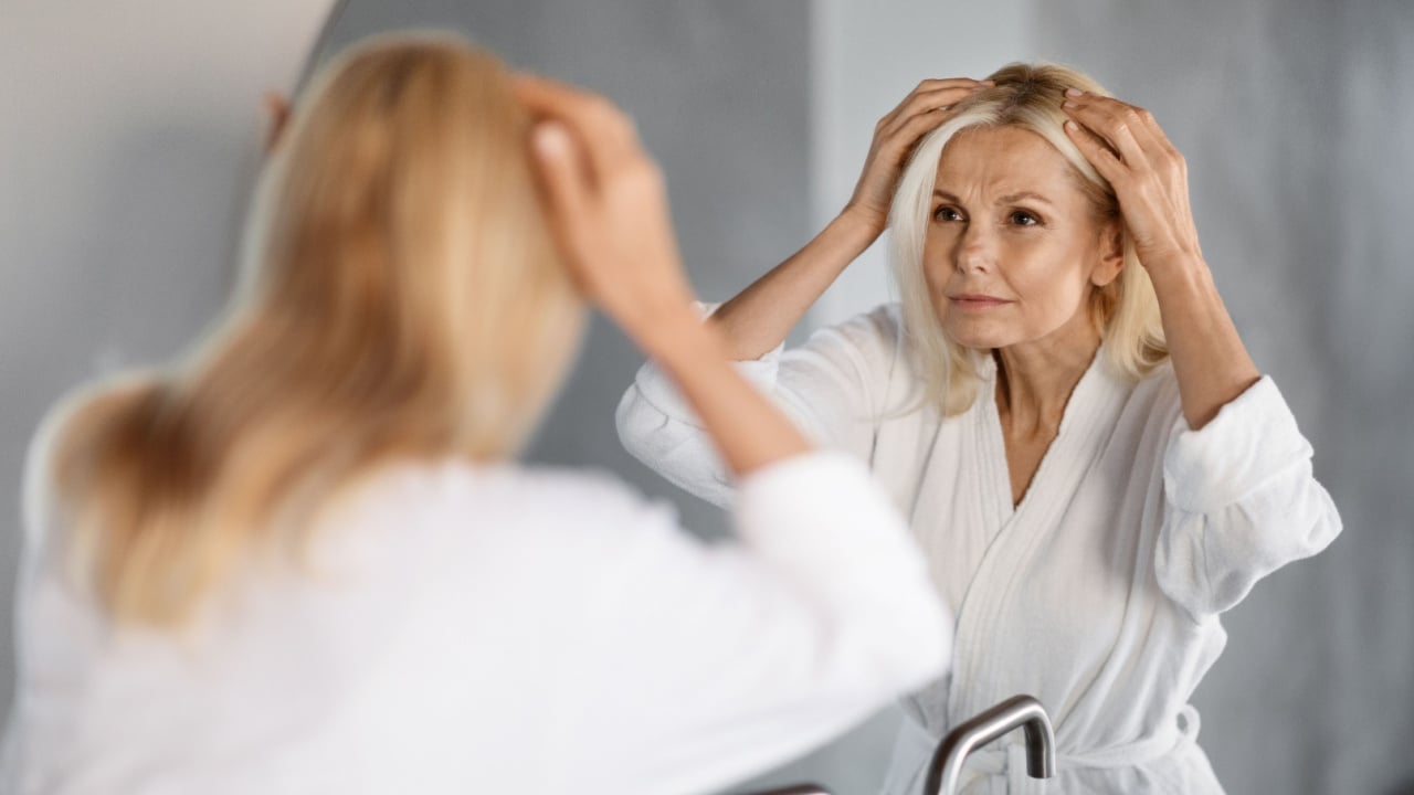 Grey Hair Concept. Upset Mature Woman Looking In Mirror At Her Hair Roots, Worried Senior Lady In Bathrobe Suffering Graying Or Hairloss Problem, Selective Focus On Reflection, Closeup Shot