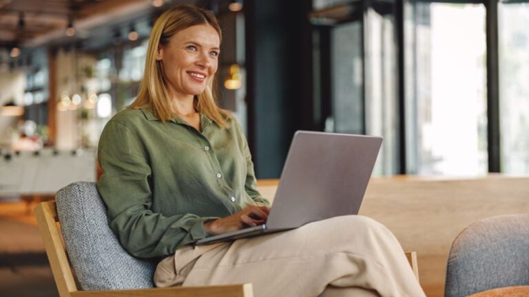 Stylish woman freelancer working on laptop in cozy coworking and looking at side