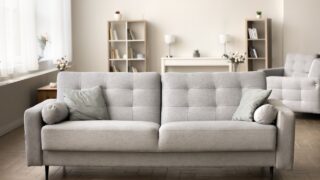 Comfortable grey couch in cozy empty living room. Modern Scandinavian interior with stylish sofa, cushions, cozy home decoration, elegant furniture in background. Real estate apartment for rent, sale
