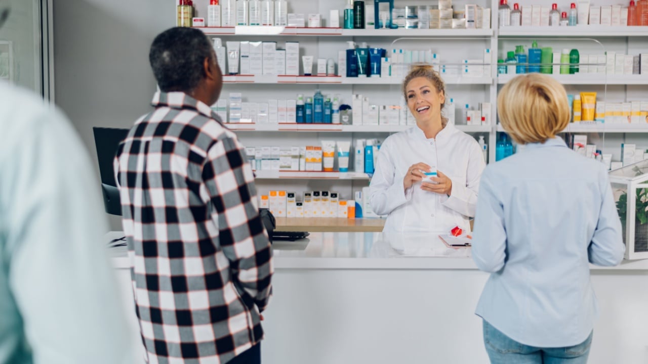 Portrait of a beautiful woman pharmacist working in a pharmacy while selling medications to customers. Young female worker wearing a white lab coat and talking to a patient in a drugstore.
