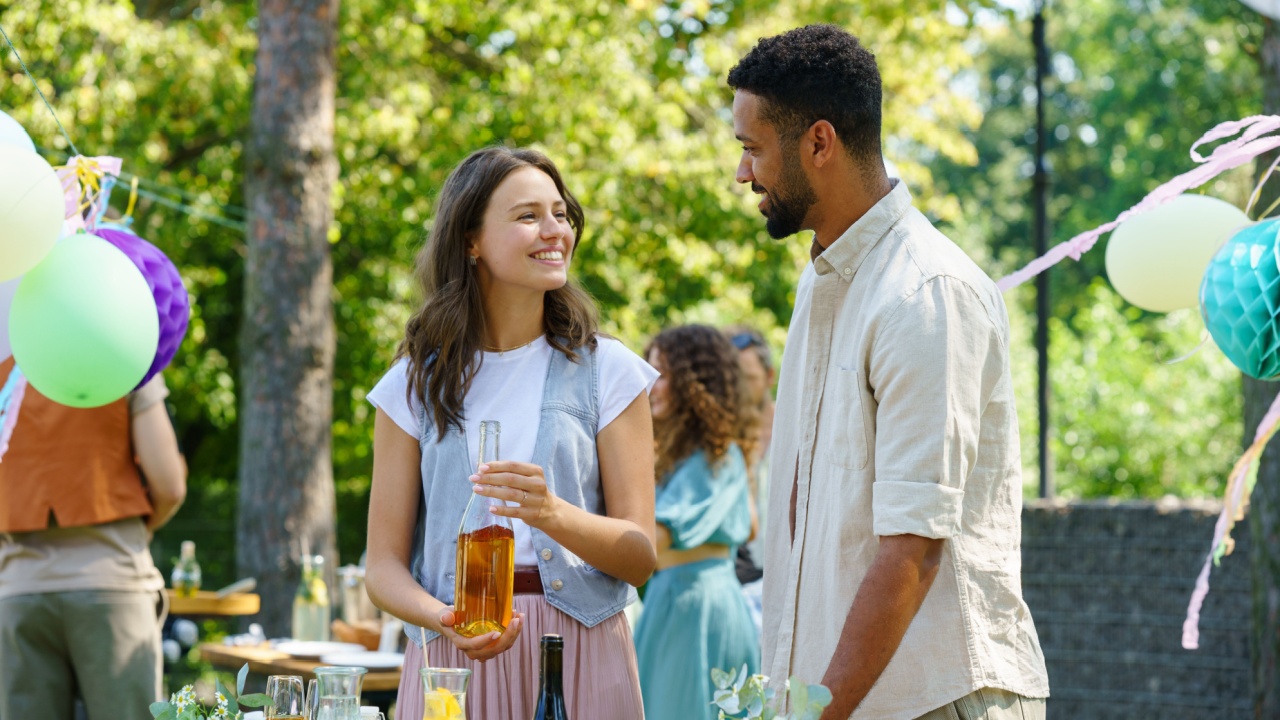 Friends talking and having fun at summer grill garden party. Multiracial couple hosting garden party.