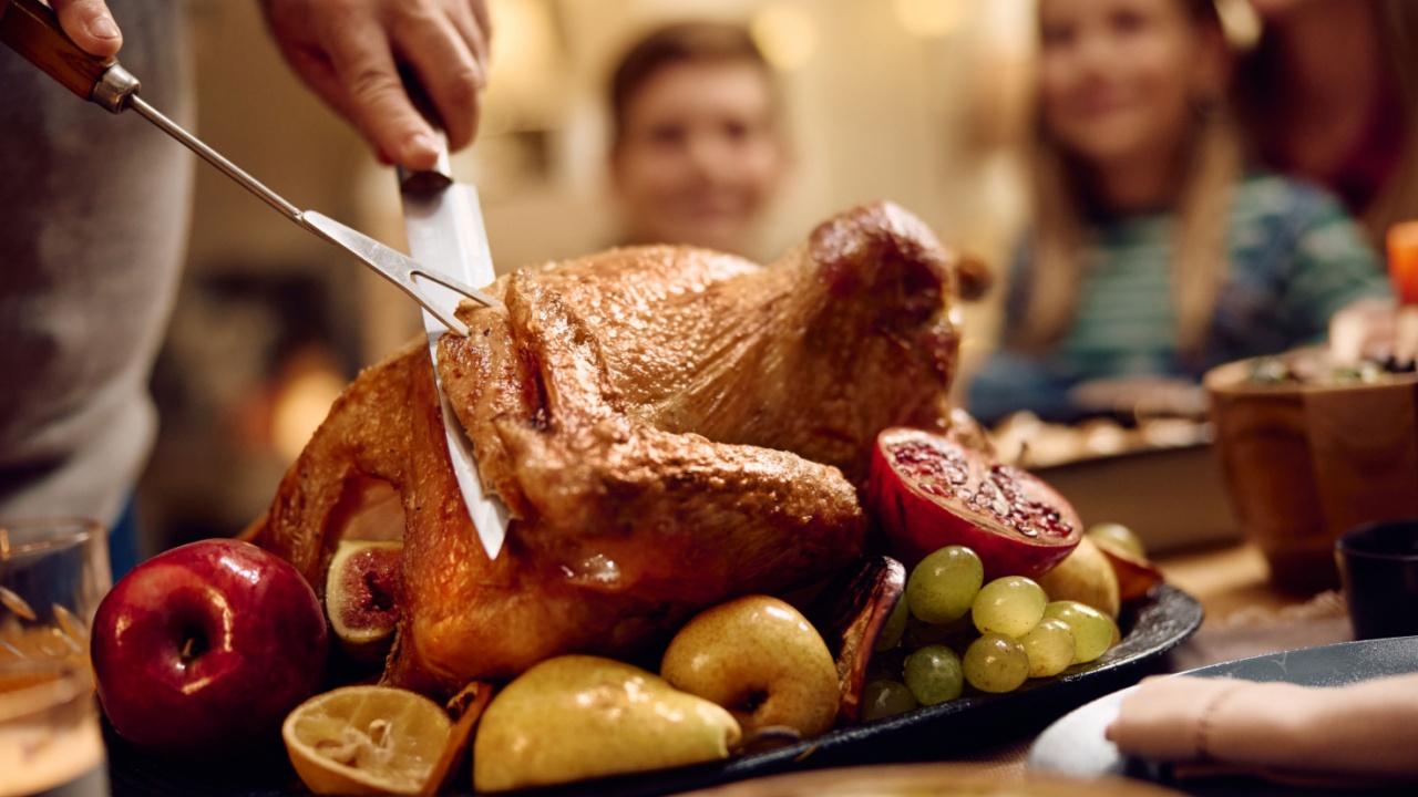 Close up of father carving roast turkey for his family during Thanksgiving dinner at dining table.