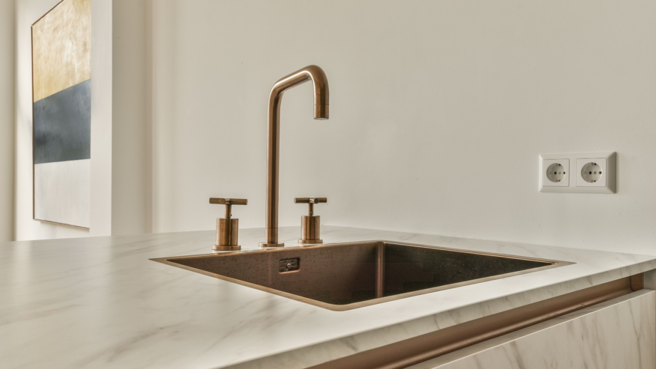 a white kitchen with marble counter top and copper fauced fae sink in the photo is taken from above