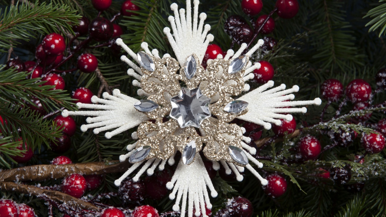 an ice flake star, a Christmas tree decoration, surrounded by fir branches and a snow-covered holly branch with red berries.