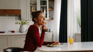 Side view of happy young woman enjoying healthy food for lunch at the domestic kitchen