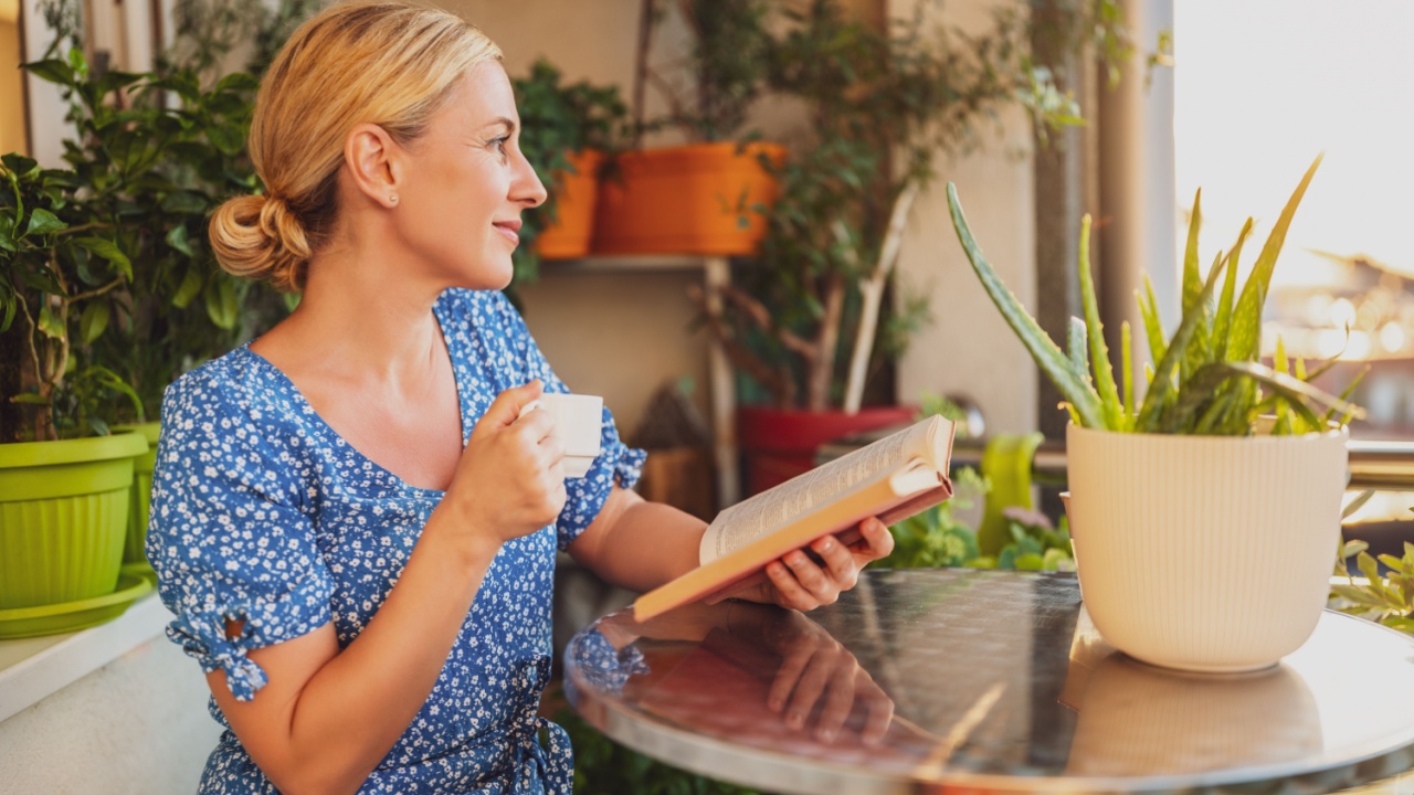 Beautiful woman enjoys reading book and drinking coffee on her balcony.