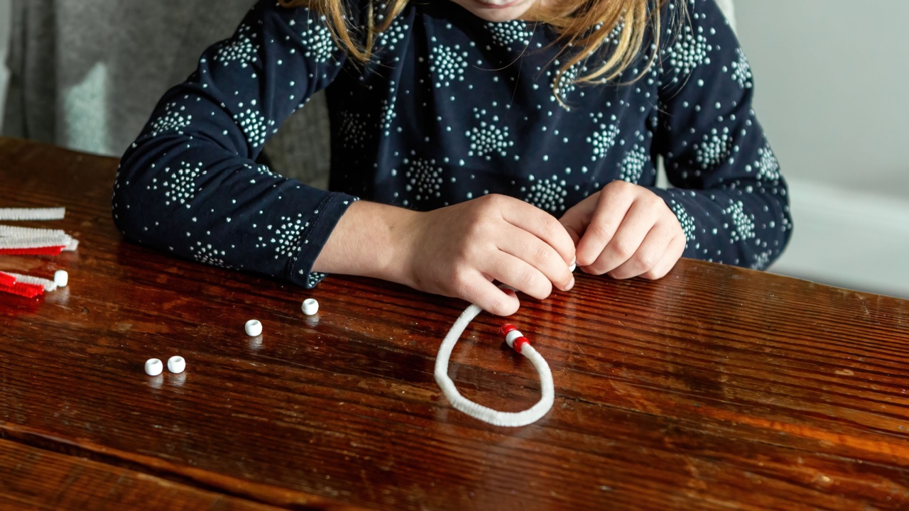 Little girls hand crafting a candy cane or bracelet with plastic beads and pipe cleaners. Made with her own hands. Children's art project. Craft forkids. Top view.