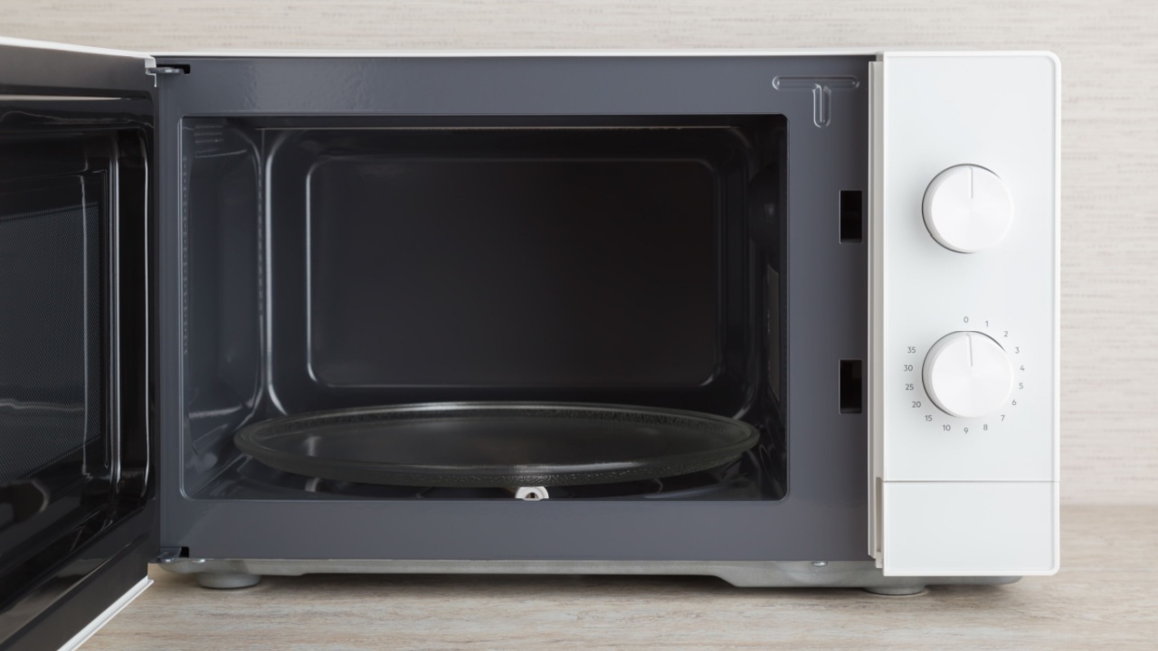 New white microwave oven with opened door on table top at home kitchen. Empty glass plate inside for food. Closeup. Front view.