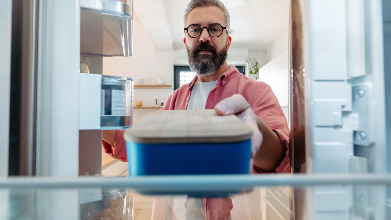 Handsome man putting lunchbox in fridge. Taking out lunch from fridge, eating leftovers. Stop trowing food away, reducting food waste.