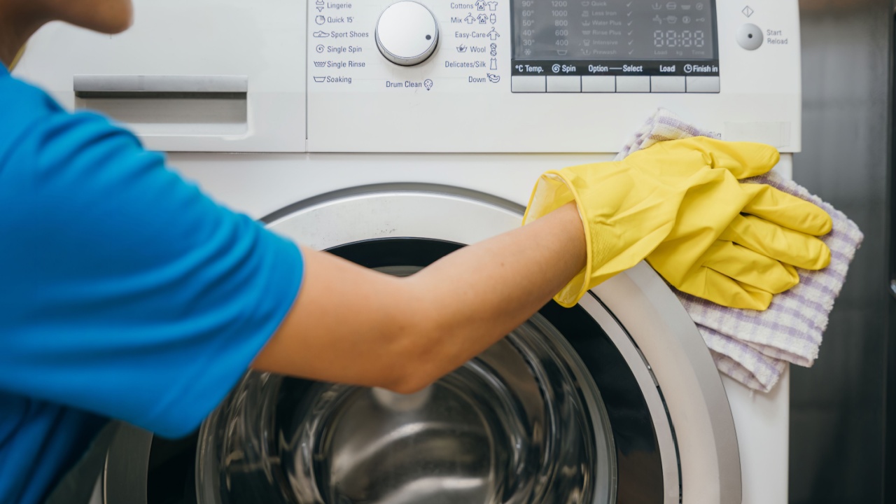 Woman in protective glove carefully cleans and wipes washing machine. Highlighting regular housework and hygiene routine. Cleaner at work glove house purity. Clean laundry. Maid Cleaning service.