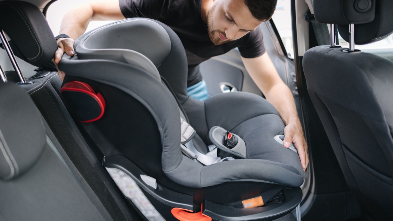 Man installs a child car seat in car at the back seat. Responsible father thought about the safety of his child. Man fasten seat belt on baby car seat