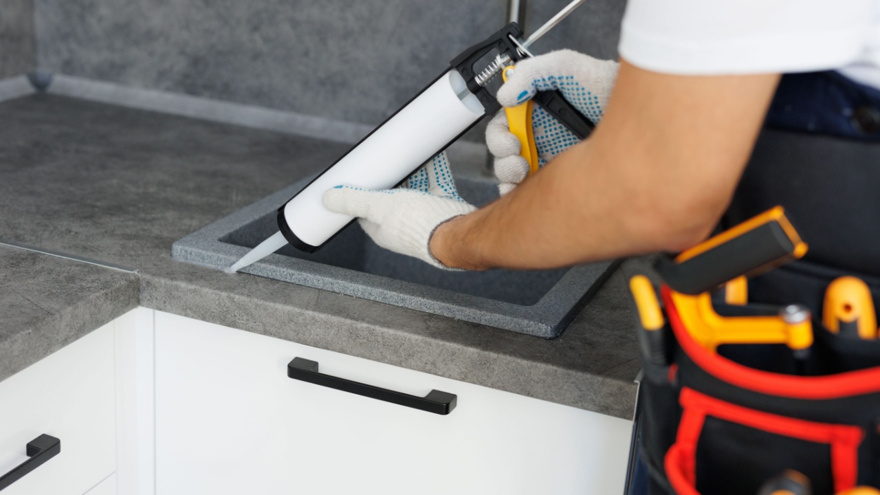 Worker seals up the kitchen sink with a sealant using a construction sealing gun