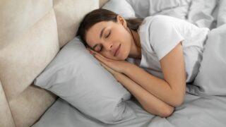 Serene young woman lies comfortably in bed, her expression tranquil as she enjoys deep, restful sleep, suggesting peace and relaxation, bedroom interior