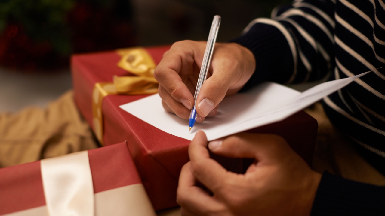Pen, hands and man with card and gift for Christmas event or party at home for family. Celebration, paper and closeup of male person writing letter with present boxes for xmas festive holiday.