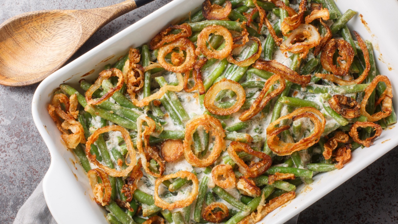 Delicious creamy Green Bean Casserole sprinkled with crispy fried onions on the baking dish on the table. Horizontal top view from above