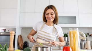 Joyful Young Lady Cooking and Sampling Dinner in a Pot, Present in a Contemporary Home Kitchen. Homemaker Preparing Nutritious Meal with a Smile. Domestic Life and Nourishment. Healthy Eating.