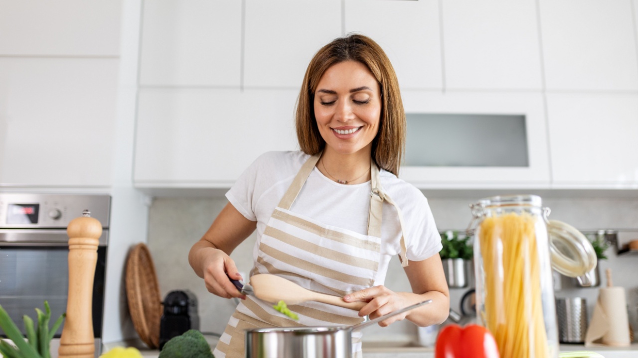 Joyful Young Lady Cooking and Sampling Dinner in a Pot, Present in a Contemporary Home Kitchen. Homemaker Preparing Nutritious Meal with a Smile. Domestic Life and Nourishment. Healthy Eating.