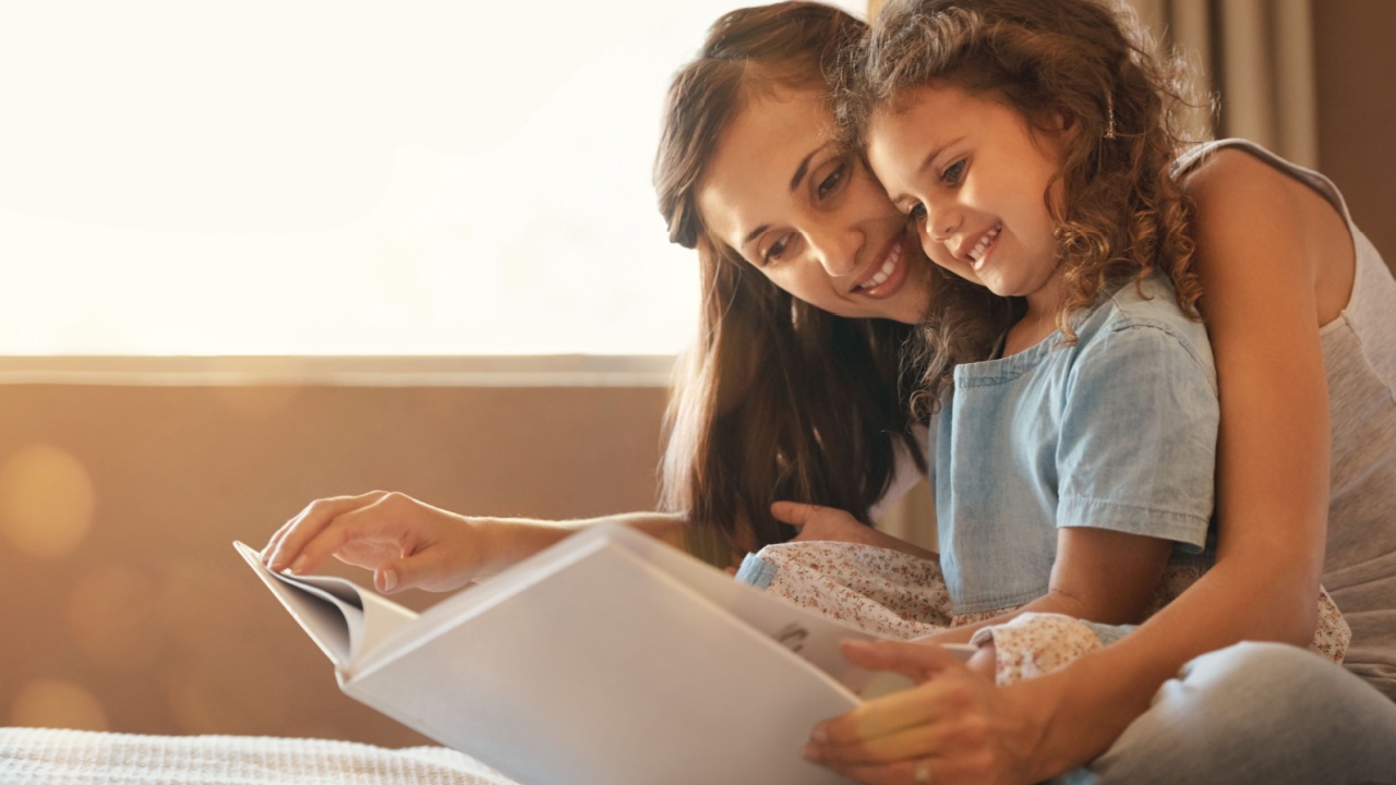 Bed, mom and daughter with book, smile and bonding for story, education and learning in home. Reading, woman and child in bedroom for storytelling, happy and relax with care, growth and development