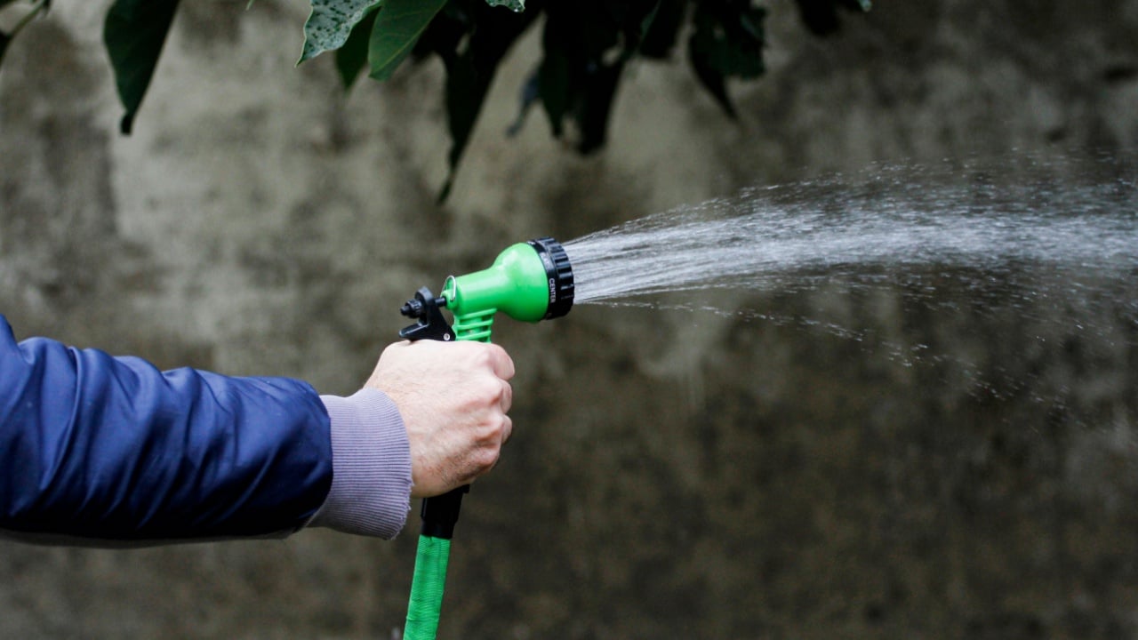 Closeup of a man&acute;s hand holding a hose and watering the garden