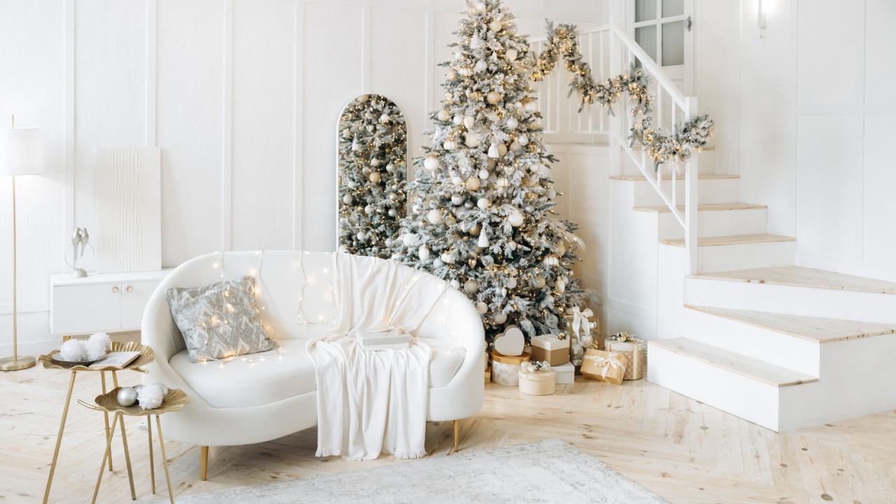 Modern living room with a Christmas tree decorated in silver and gold, white sofa with cushions and a blanket, gifts under the tree. The room exudes holiday warmth and cheer