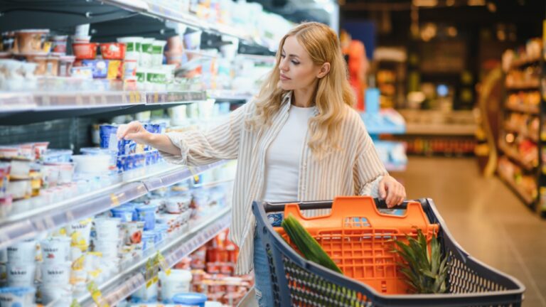 Young adult woman pushing shopping trolley between the shelves in the market.