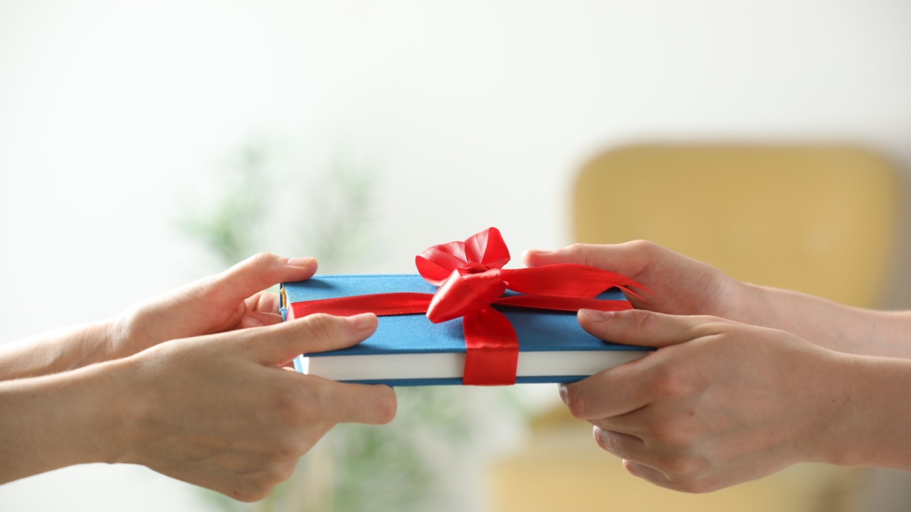 Woman gifting her friend book tied with red ribbon indoors, closeup