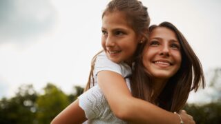 Outdoor, piggyback and sister with smile, child and bonding in nature, thinking and happy in forest. Love, girls and fun in woods, carrying and teenager with care for kid, siblings and contemplating