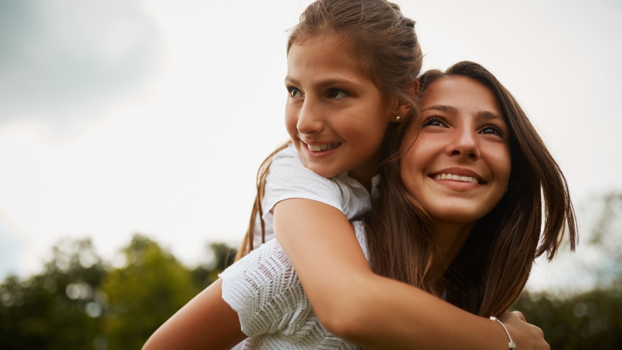 Outdoor, piggyback and sister with smile, child and bonding in nature, thinking and happy in forest. Love, girls and fun in woods, carrying and teenager with care for kid, siblings and contemplating
