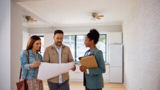 Mid adult couple examining housing plans with their real estate agent while buying new home.
