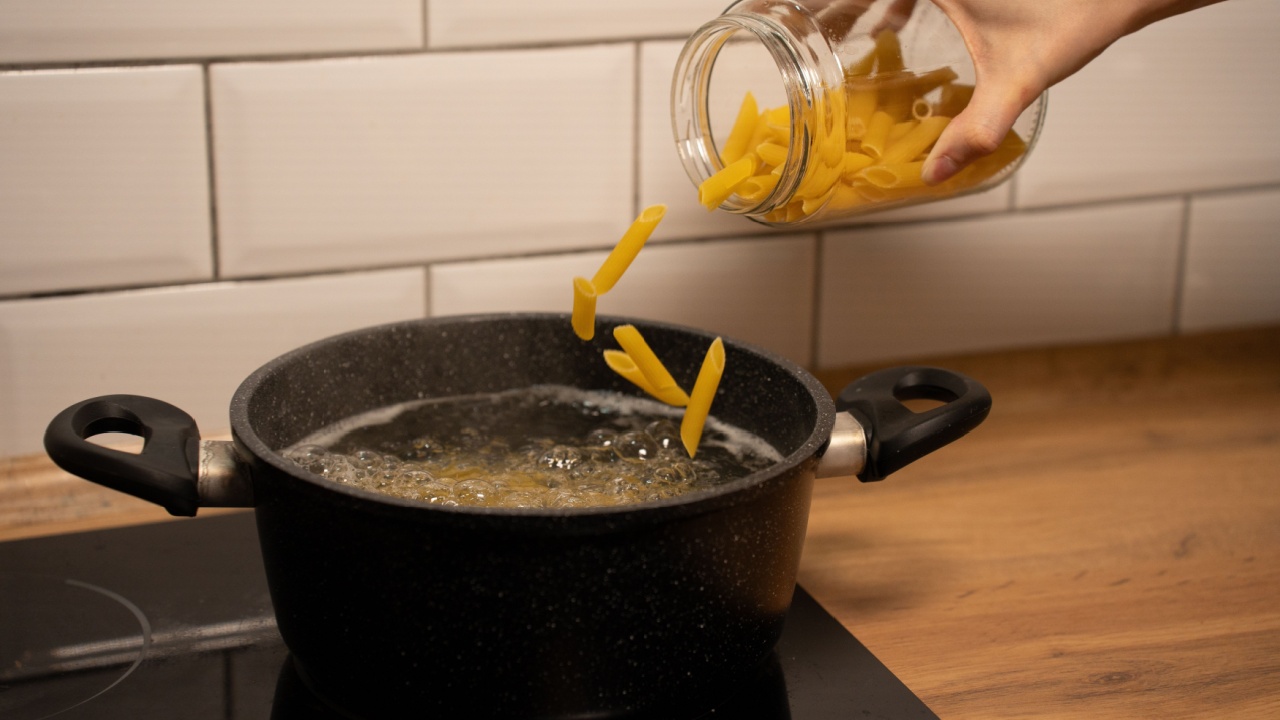 The cooking process at home, a saucepan on the stove, boiling water, pasta in a glass container. The pasta is flying into the pan. 