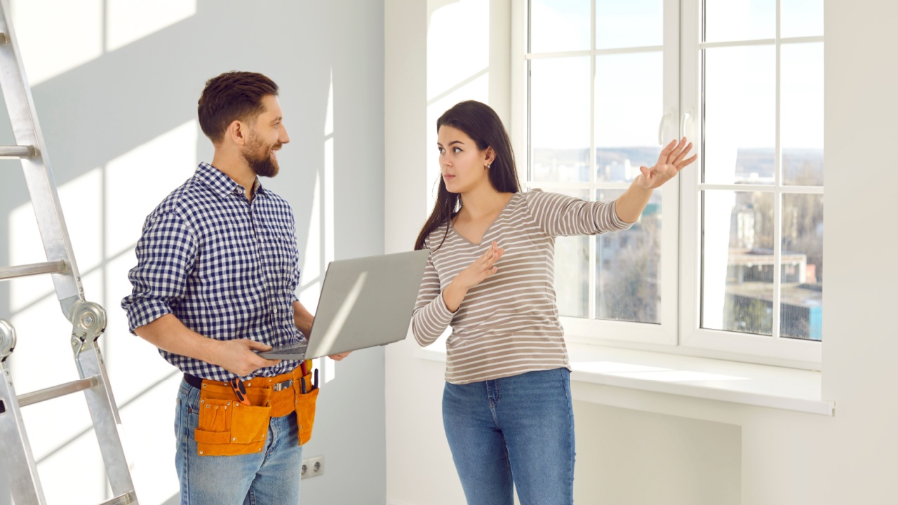 Young woman talking to a repairman who is going to make repairs in her house. Workman with a tool belt and laptop listening a girl homeowner explaining to him what work she needs to done at home