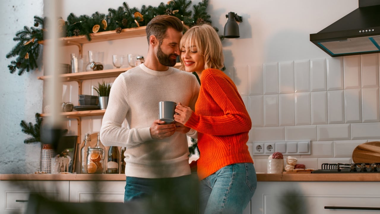 A joyful couple deeply in love shares a warm and intimate moment in a beautifully decorated kitchen during the enchanting holiday season, embodying the true essence of winter coziness and happiness