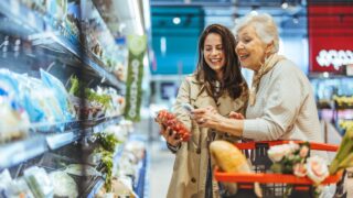 A joyful senior woman and young woman shopping for fresh groceries together in a supermarket, enjoying quality time and bonding while choosing produce and essentials.