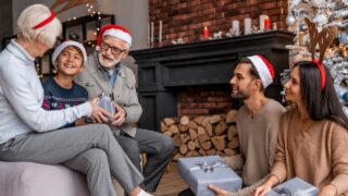 Happy young family sitting together in living room on Christmas eve and exchanging present boxes. Happy New Year Eve! Family reunion for winter holiday spirit