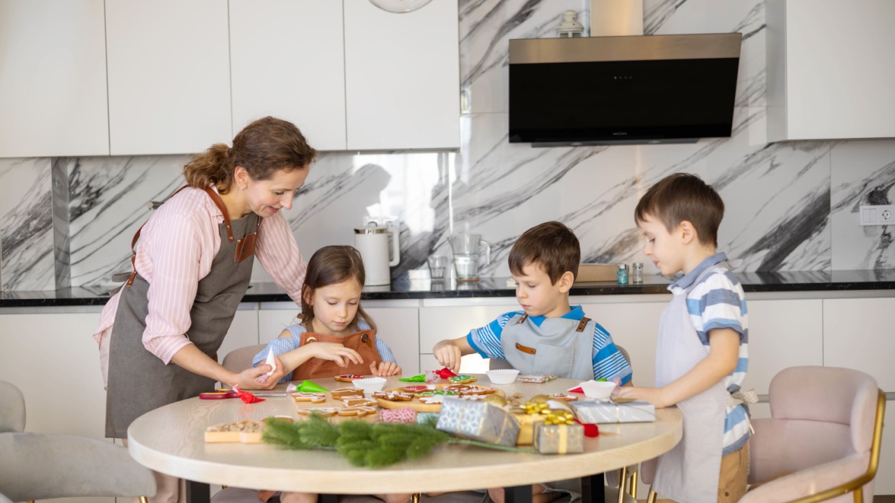 Happy family mother and children in aprons making Christmas cookies together while cooking in kitchen at home, smiling little children helping mom to decorate xmas gingerbreads during winter holidays