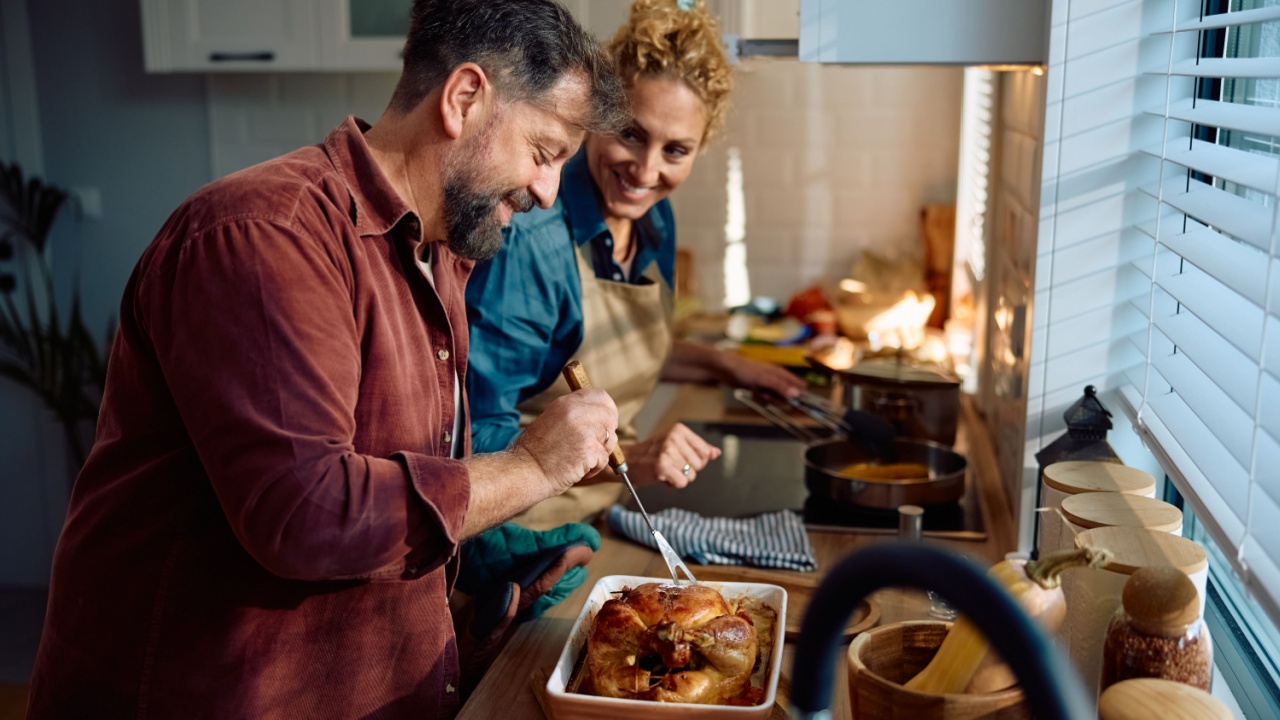 Happy man and his wife preparing roast turkey for Thanksgiving meal while cooking together in the kitchen.