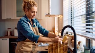 Smiling woman cleaning wooden cutting board under the sink after preparing food in the kitchen.